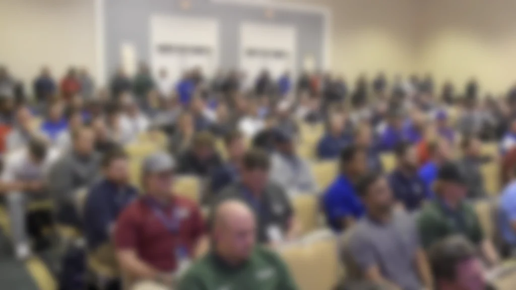Coaches sit in a lecture room listening to a speech